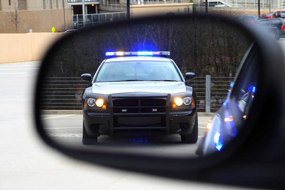 Cop car in rear view mirror pulling over for disobey sign ticket in Ontario